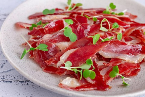 Ham of duck breast, dried duck fillet, with microgreens, plate, on a tiled table