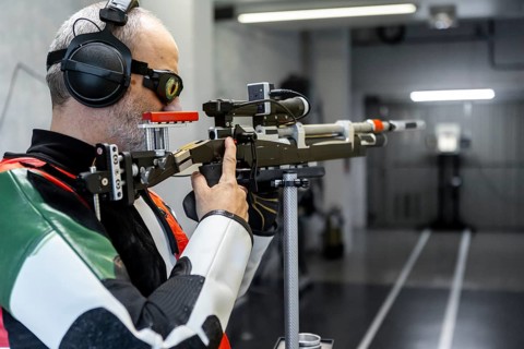 A blind athlete in Paralympic shooting attire focuses on aiming during a training session. The