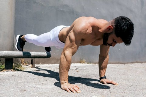 Athletic man demonstrating strength and fitness by performing a push-up outdoors on concrete,