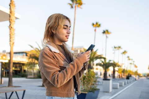 Mixed-race woman in casual jacket using a smartphone outdoors She appears to be busy with the