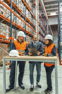 Warehouse workers and manager discussing logistics using a clipboard in a large distribution center