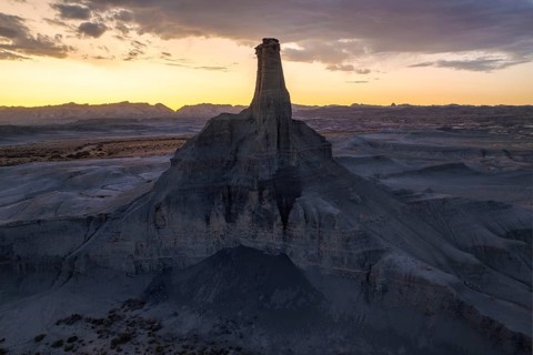 A breathtaking view of the sun setting behind a towering rock formation in the desolate landscape