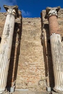 Low angle view of old terracotta brick and stone wall remnants framed by marble columns with carved