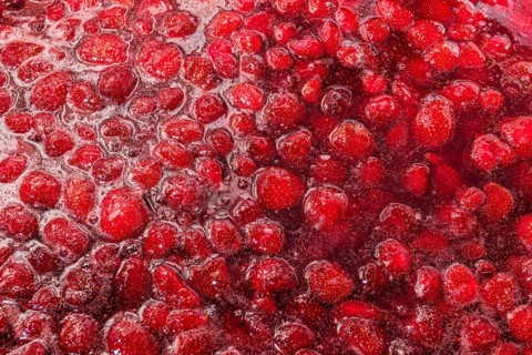 A close up image of vibrant homemade strawberry jam, showcasing the rich texture and color of fresh