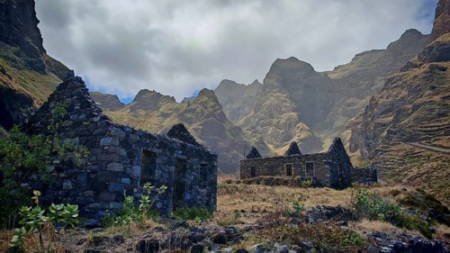 Stone ruins of old houses made of volcanic stone against a spectacular mountain backdrop with thick