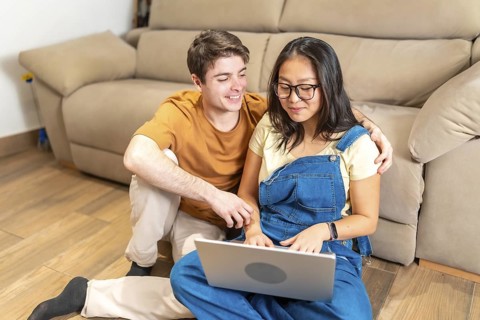 Young multiethnic couple sitting on the floor and using a laptop, browsing internet or working from