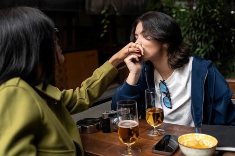 A lesbian couple enjoys a tender moment at a café, where one woman gently kisses the other's hand.