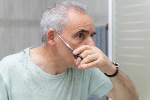 A man carefully trims his own hair using scissors in front of a bathroom mirror. The image