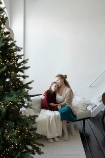 A mother and daughter share a tender moment, embracing on a cozy sofa next to a decorated Christmas