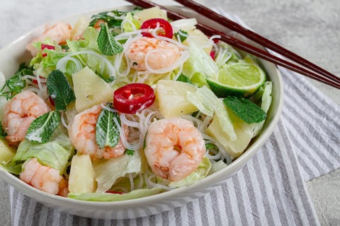 Thai salad with shrimp and rice noodles, pineapple slices, coriander and mint leaves, on a white