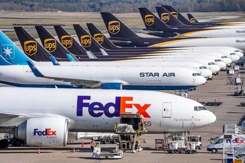 FedEx Express Boeing 777-FS2 cargo plane is unloaded, air freight container, behind cargo fleet of