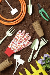 A flat lay of gardening tools including gloves, trowel, hose, and pots on rich soil, symbolizing