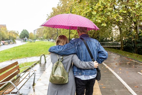 A couple with intellectual disabilities walks arm in arm under a pink polka dot umbrella on a rainy