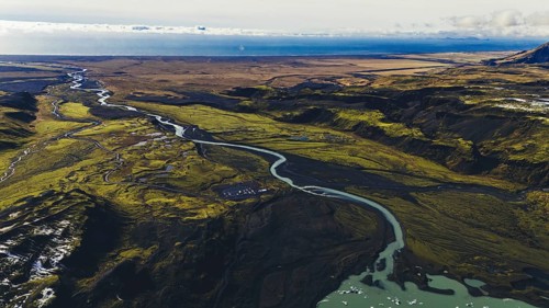 Wide aerial view of braided rivers flowing through mossy and volcanic terrain in southern Iceland,