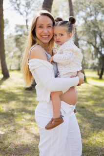 A joyful pregnant mother holds her young daughter outdoors, surrounded by nature. They are enjoying