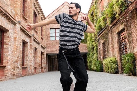 A Cuban man passionately dances in a vibrant urban courtyard, surrounded by brick buildings and