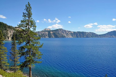 Tranquil landscape with deep blue lake surrounded by green trees and mountainous backdrop under a