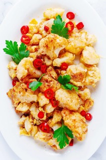 Cauliflower dish, with chili pepper and parsley, on a white plate served on a marble countertop