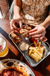 Chicken wings served with dips alongside crispy fries and a pizza. Accompanied by a refreshing