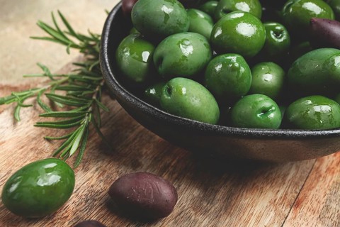 Chalkidiki olives, classic Greek green olives, in a bowl on a cutting board, top view, without