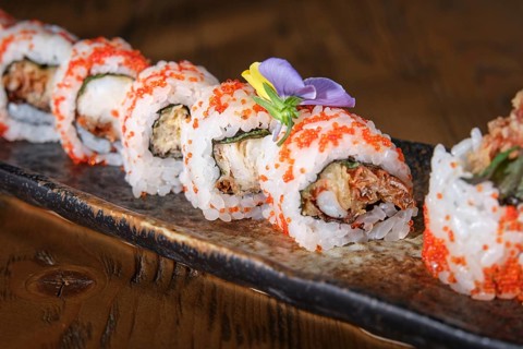 Delicious soft shell crab uramaki sushi rolls are garnished with masago and edible flowers, plated