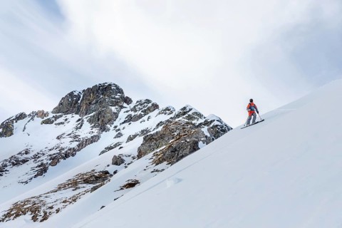 A lone skier ascends a snow-covered mountain, showcasing the thrill of ski touring. The bright sky