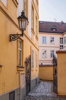 Quaint alleyway flanked by yellow buildings in Prague, featuring an ornate lantern and wrought iron