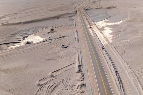 Aerial view of a long, solitary asphalt road cutting through an expansive desert landscape of the