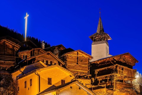 Old farmhouses and barn barn, in the back the illuminated cross and the illuminated church tower of