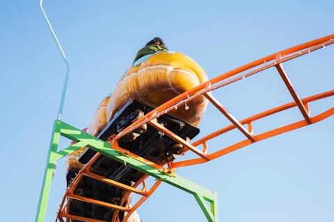 Close-up of a roller coaster ride on a bright orange track, set against a clear blue sky, capturing