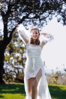A bride in a white dress stands beautifully in a sunlit garden of an ancient villa in Treia,