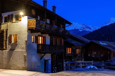 Old illuminated farmhouses in Rue du Village, night view, historic town center, Grimentz, Val