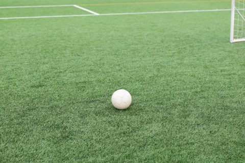 A close up shot of a soccer ball resting on a lush green field with a soccer goal in the