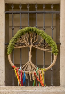 A peace wreath made of rope and moss with colourful ribbons hangs in front of a window grille