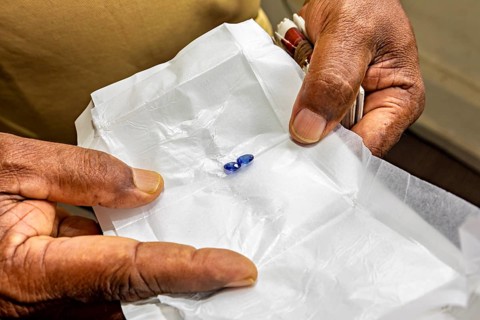 Two precious stones on white paper, held by hands. Focus on craftsmanship and detail, the sapphire
