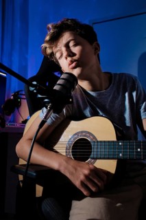 A young musician passionately sings into a microphone while playing an acoustic guitar in home