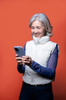 Asian Chinese senior woman enjoying technology as she smiles at her smartphone. Wearing a casual