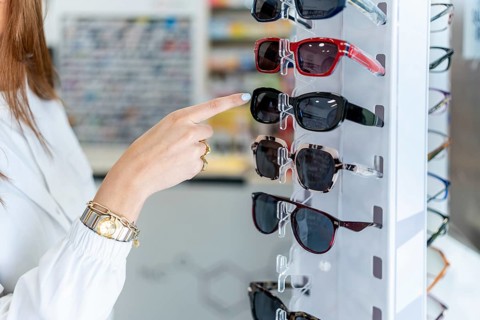 Woman's hand pointing to stylish sunglasses on a white display stand in a pharmacy, selecting