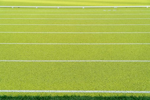 Close-up of vibrant green synthetic running track with white lanes in an outdoor athletics stadium.
