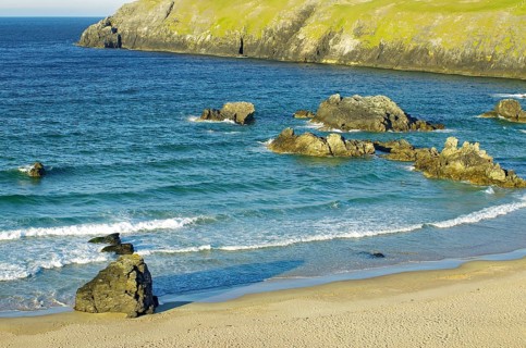 Rocky coastline with blue sea, breaking waves and huge rocks under clear skies, Durness, Highlands,