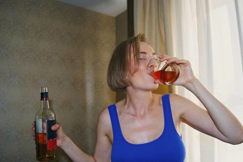 A woman is captured in a dynamic moment as she enjoys a glass of whiskey at home, dancing