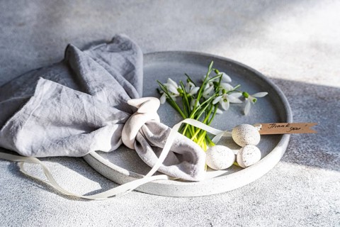 A plate elegantly displays spring snowdrops alongside speckled Easter eggs, a grey linen cloth, and