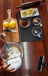 A woman prepares cookie dough for baking in a glass container on a wooden table, surrounded by