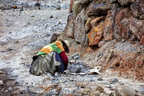A person wearing colorful clothes works in a rocky environment, the Potosi silver mines on Cerro