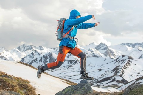 A man skillfully navigates rocky terrain in the snowy Pyrenees. Dressed in dynamic outdoor gear, he