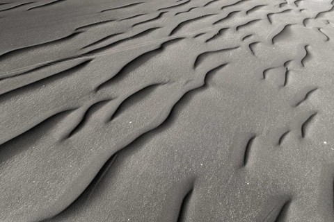 Richly textured black sand forms intricate designs, showcasing the interplay of natural elements
