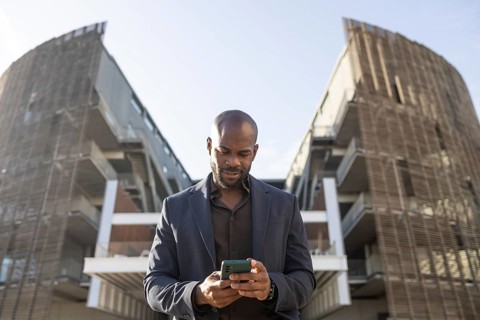A business cuban man checks his smartphone in front of a contemporary architectural structure. He