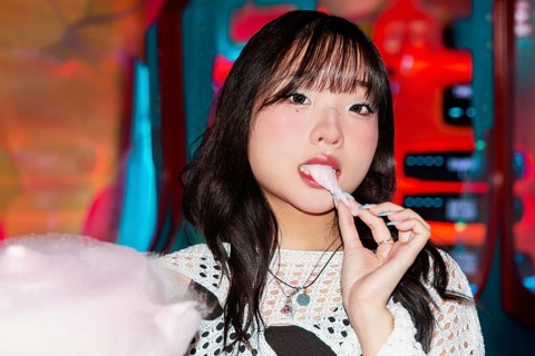 An Asian Gen Z girl enjoys cotton candy at a bright, colorful arcade She displays a sense of