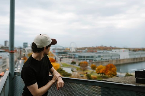 Side view of unrecognizable man in cap overlooking autumn-hued Montreal cityscape from a high