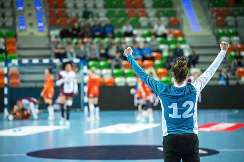 Handball woman goalkeeper's victory gesture and handball match in the background